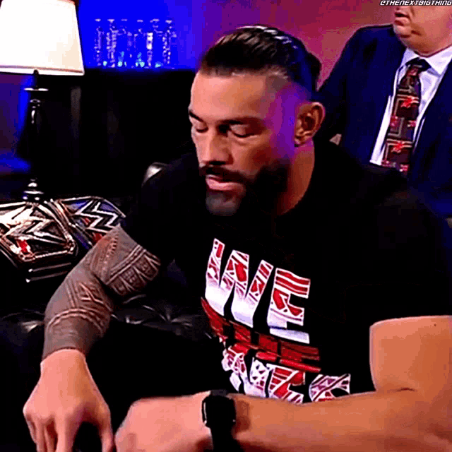 a man wearing a black shirt with the word love on it is sitting on a couch .