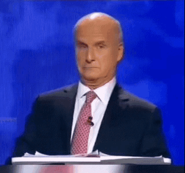 a man in a suit and tie stands at a podium with a blue background