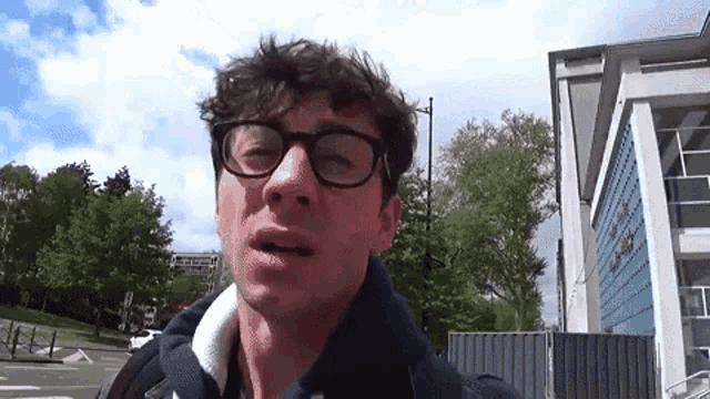 a man wearing glasses is standing in front of a building that says ' a ' on the front