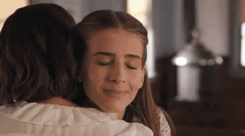 a woman is hugging a young girl with her eyes closed and smiling .