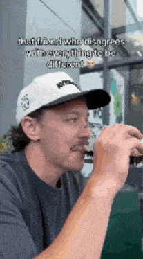 a man wearing a hat is drinking from a cup and says that friend who disagrees with everything to be different