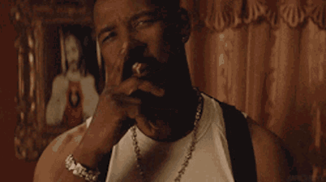 a man with a beard is wearing a white tank top and a chain around his neck