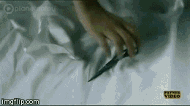 a person is laying on a bed holding a knife .