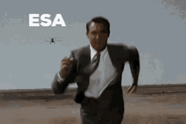a man in a suit and tie is running in the desert with a plane flying in the background that says esa