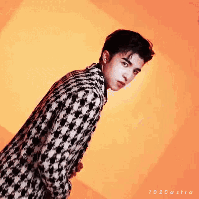 a young man in a black and white plaid jacket is standing in front of an orange background .