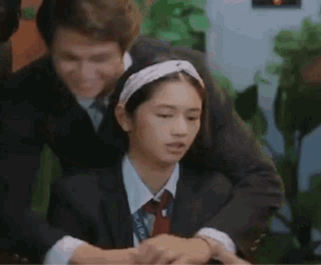 a man and a woman are sitting next to each other . the woman is wearing a headband and a tie .