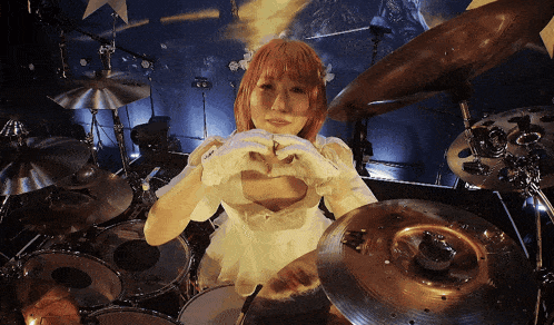 a woman is making a heart with her hands in front of a drum set