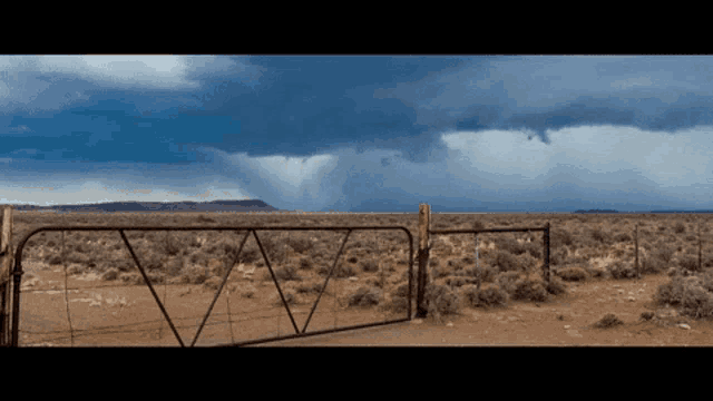 a fence in the middle of a desert with a cloudy sky behind it