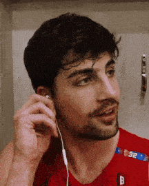 a man wearing a red shirt with the letter b on it adjusts his ear buds