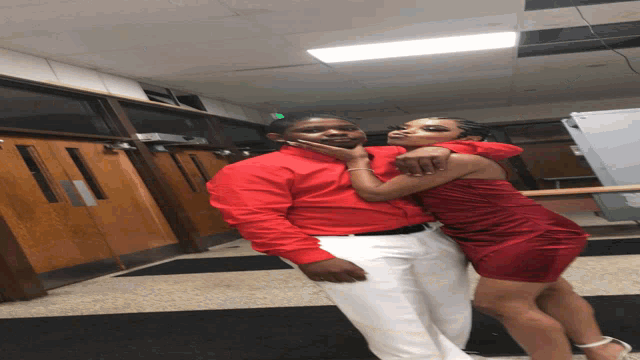 a man in a red shirt holds a woman in a red dress on his shoulders