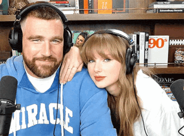 a man wearing a blue miracle sweatshirt stands next to a woman wearing headphones and a microphone