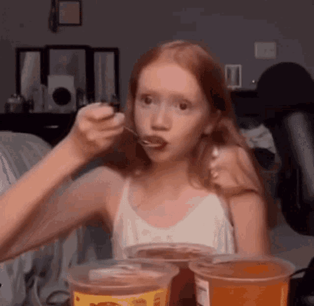 a young girl is eating a spoonful of food from a plastic container .