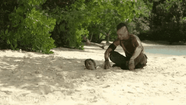 a man is kneeling on a sandy beach looking at another man 's head