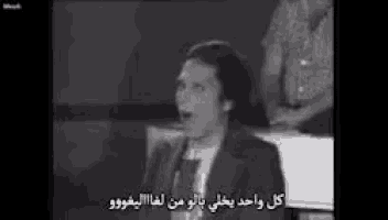 a black and white photo of a man in a suit and tie speaking in arabic .