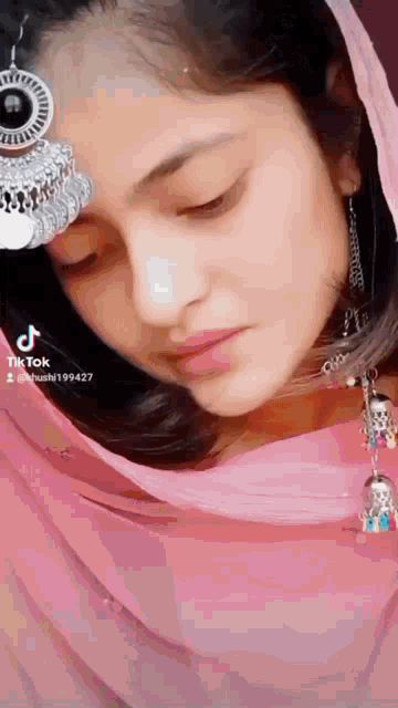 a close up of a woman wearing a pink scarf and earrings with her eyes closed .