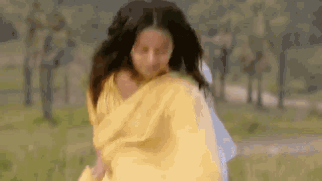 a woman in a yellow saree is dancing in a field .