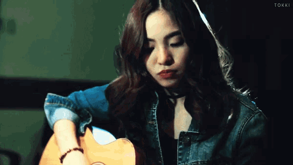 a woman in a denim jacket is holding a guitar and the word tokki is visible in the corner