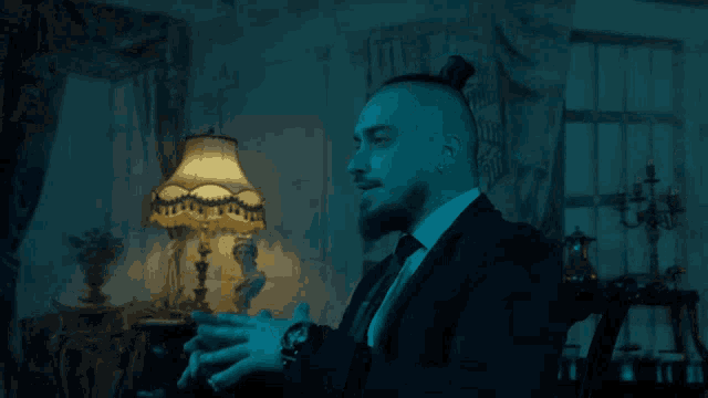 a man in a suit and tie is sitting in front of a lamp