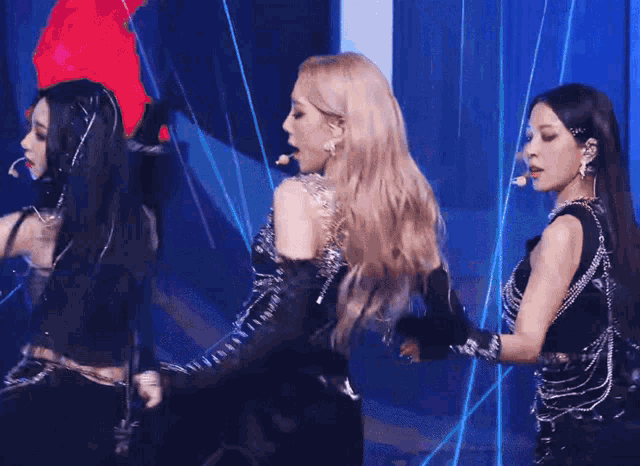 a group of women are standing on a stage and one has a microphone in her mouth