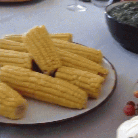 a white plate topped with corn on the cob and a bowl of spinach