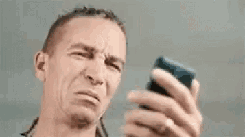 a man is making a funny face while looking at a cell phone .