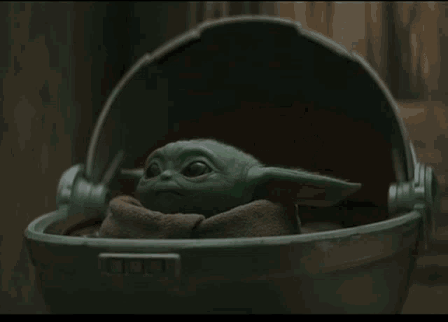 a baby yoda is wrapped in a blanket and sitting in a cradle