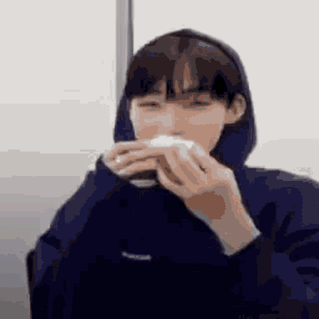 a person wearing a blue hoodie is eating a sandwich .