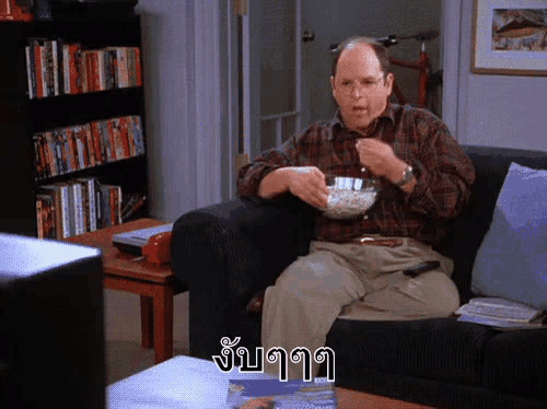 a man sitting on a couch with a bowl of popcorn in front of a bookshelf with foreign writing