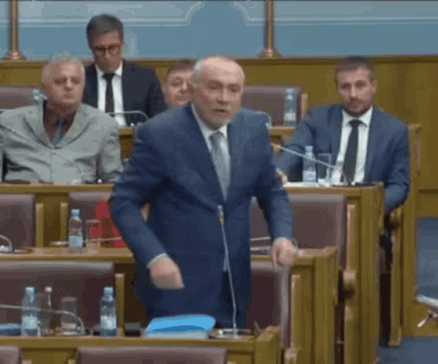 a man in a suit and tie stands in front of a microphone in a parliament