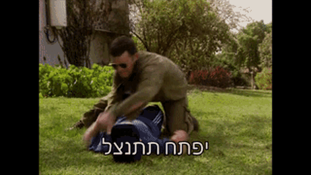 a man in a military uniform is kneeling down in the grass with a man laying on the ground behind him .