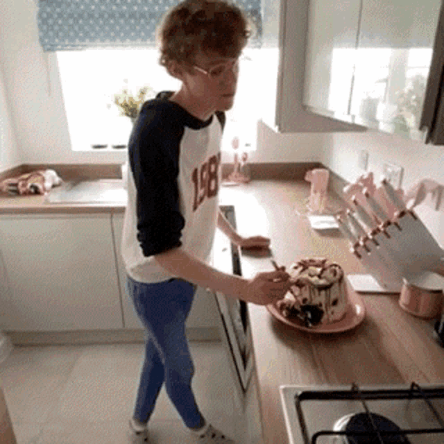 a young man wearing a shirt with the number 198 on it is cutting a cake in a kitchen .