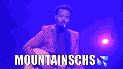 a man in a plaid shirt is playing a guitar and the words mountainschs are above him