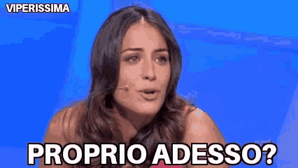 a woman is talking into a microphone with the words proprio adesso written below her