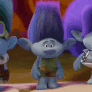 a troll with blue hair and a green shirt is standing next to two other trolls .
