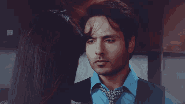 a man wearing a blue shirt and tie looks at a woman