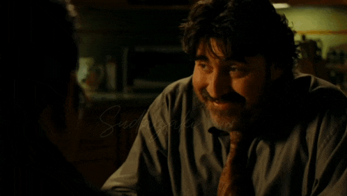 a man with a beard is smiling in a dark room with the word swank written in the corner
