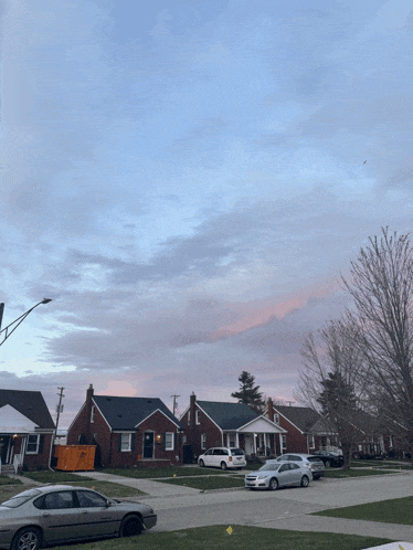 a row of houses with cars parked in front of them and a yellow dumpster