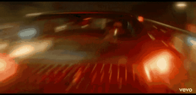 a red car is driving down a street at night with a blurry background .