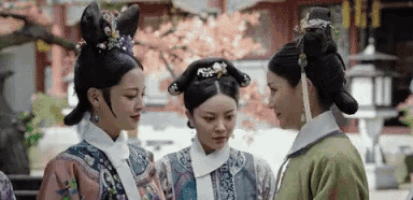 three women in traditional clothes are standing next to each other and talking .