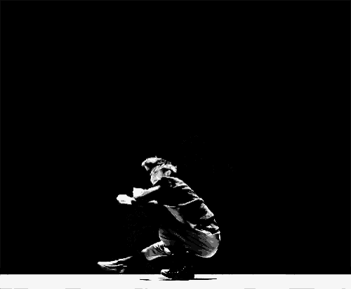 a black and white photo of a man squatting on the floor in a dark room .