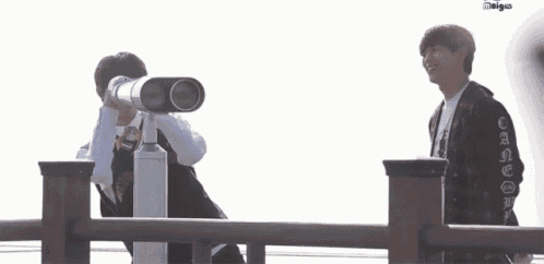 two young men are looking through a telescope on a railing .