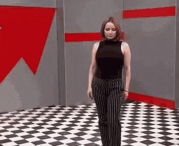 a woman in a black tank top and striped pants is standing on a checkered floor in a room .