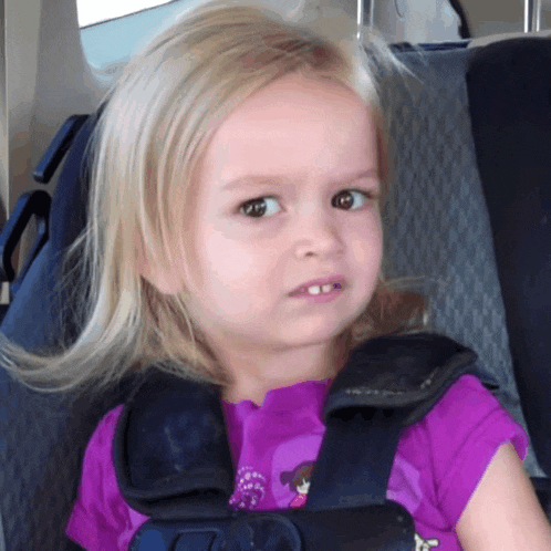 a little girl wearing a purple shirt and a seat belt looks at the camera