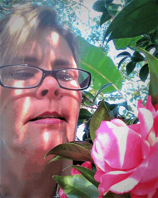 a woman wearing glasses looks at a pink flower
