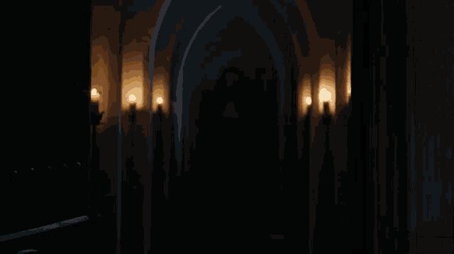 a dark hallway with candles on the walls and arches