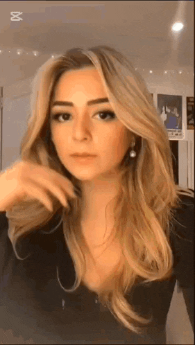 a woman with long blonde hair and earrings is wearing a black shirt and earrings .
