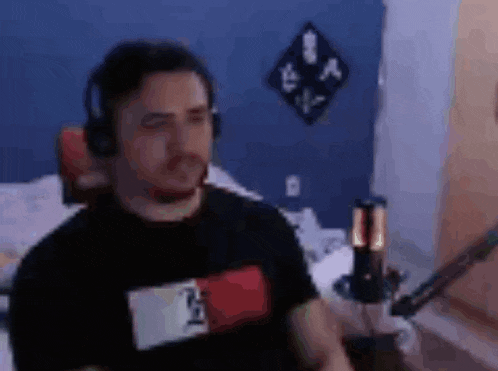 a man wearing headphones and a tommy hilfiger shirt is sitting in front of a microphone in a room .