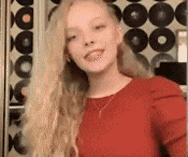 a woman with long blonde hair is wearing a red shirt and a necklace .