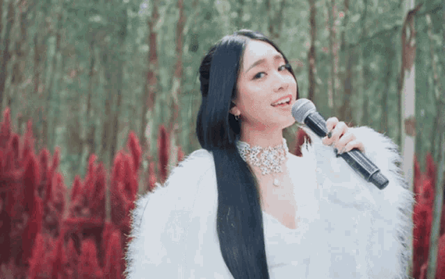 a woman with long black hair is singing into a microphone in front of red flowers