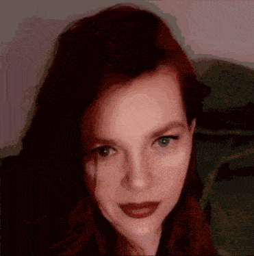 a woman with red hair and green eyes is looking at the camera